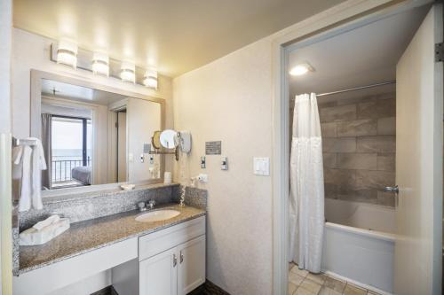 a bathroom with a sink and a mirror and a tub at Four Sails Resort in Virginia Beach