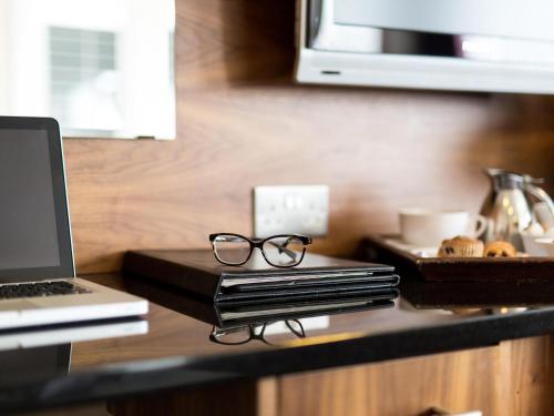 a desk with a laptop and glasses on it at Mercure Newcastle George Washington Hotel Golf & Spa in Newcastle upon Tyne