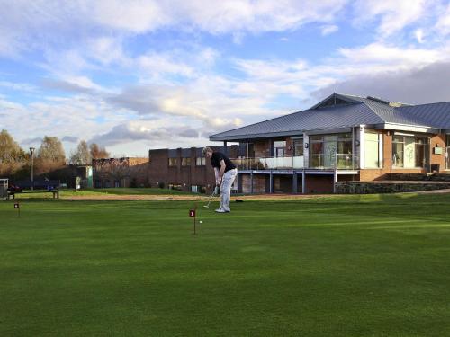 a man is playing golf on a green at Mercure Newcastle George Washington Hotel Golf & Spa in Newcastle upon Tyne