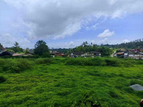a field of green grass with houses in the background at Misty Homes in Madikeri