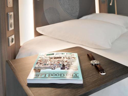 a book and a watch sitting on a table next to a bed at Novotel Avignon Centre in Avignon