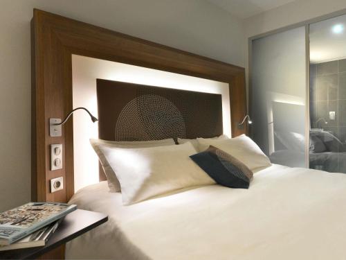 a bedroom with a white bed with a large headboard at Novotel Avignon Centre in Avignon
