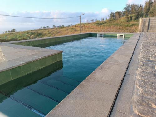 a swimming pool with blue water and a stone wall at Oak Tree House- Ponta do Pargo in Lombada Velha