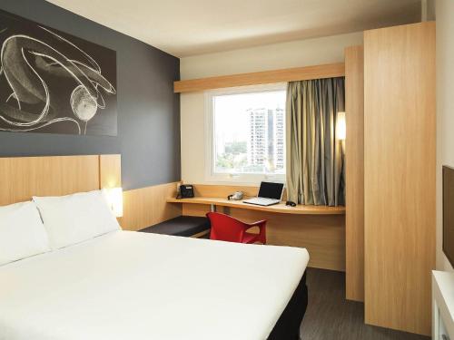 a room with a bed and a desk with a laptop at ibis Mogi das Cruzes Shopping in Mogi das Cruzes