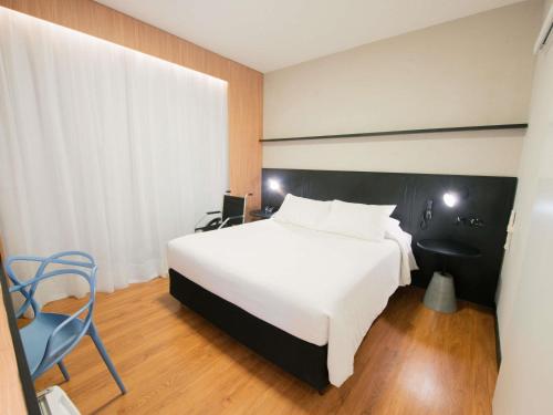a bedroom with a large white bed and a chair at ibis Curitiba Shopping in Curitiba