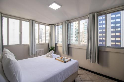 1 dormitorio con cama blanca y ventanas grandes en CLR81 - Calçadão, 1 Dorm Climatizado, Garagem, en Balneário Camboriú