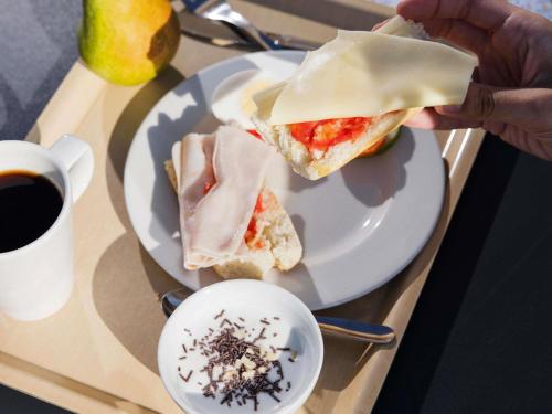 a person eating a sandwich on a plate with a cup of coffee at Ibis Budget Sevilla Aeropuerto in Seville