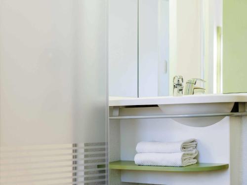 a bathroom with a sink and towels on a shelf at ibis Budget Brussels South Ruisbroek in Ruisbroek