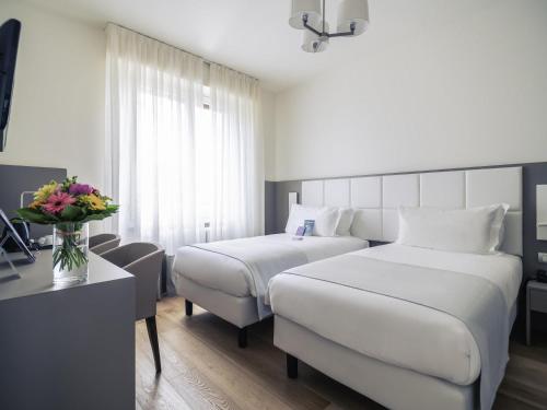 a hotel room with two beds and a table with flowers at Hotel Mercure Milano Solari in Milan