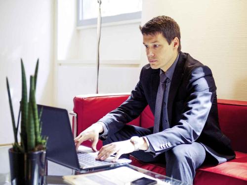 a man sitting on a couch using a laptop computer at Hotel Mercure Milano Solari in Milan