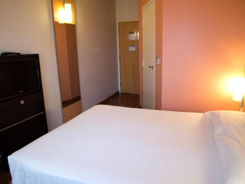a bedroom with a white bed and a flat screen tv at ibis Contagem Ceasa in Contagem