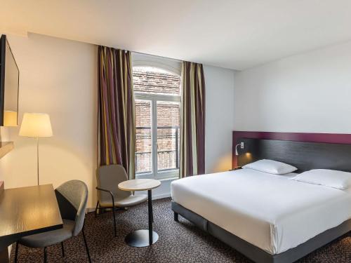 a hotel room with a bed and a desk and a window at Mercure Lille Roubaix Grand Hôtel in Roubaix