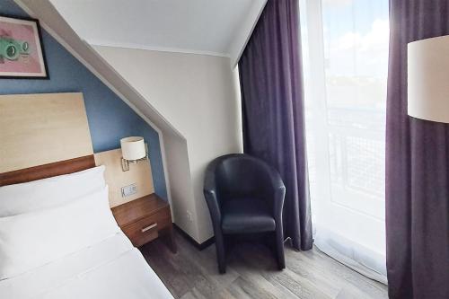 a bedroom with a bed and a chair next to a window at Garner Hotel Cologne Porz - Airport by IHG in Cologne