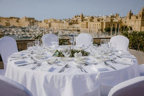 a table with white chairs and plates and forks and knives at Cugo Gran Macina Malta in Senglea