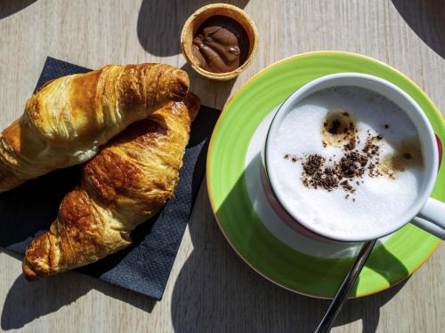 a plate with a cup of coffee and a croissant at ibis Styles Karlsruhe Ettlingen in Ettlingen
