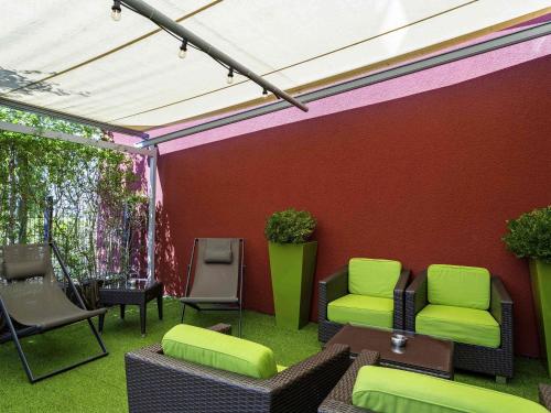a patio with green chairs and a red wall at ibis Styles Karlsruhe Ettlingen in Ettlingen