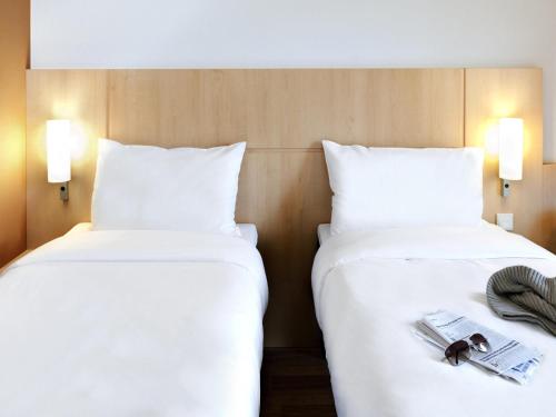 two beds in a hotel room with white sheets at ibis München City Süd in Munich