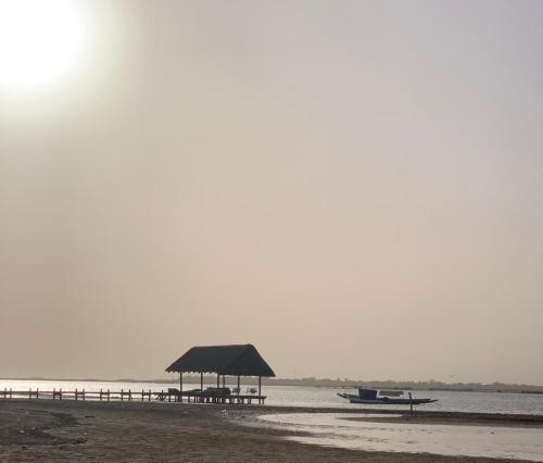 a beach with a pavilion and a pier and a boat at Diam Bougoum à MAR LODJ in Fimela