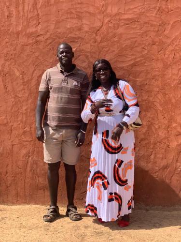 a man and a woman standing next to a red wall at Diam Bougoum à MAR LODJ in Fimela