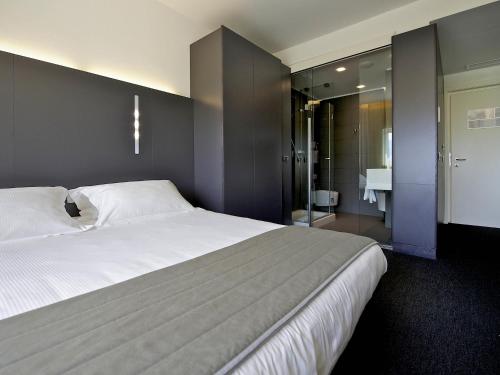 a bedroom with a large white bed and a bathroom at Mercure Nerocubo Rovereto in Rovereto
