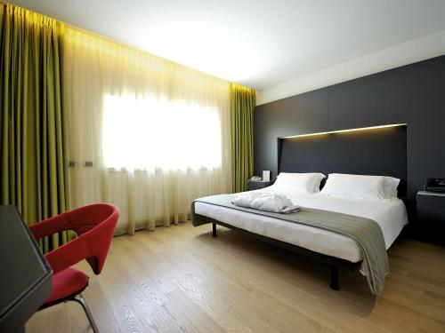 a bedroom with a large bed and a red chair at Mercure Nerocubo Rovereto in Rovereto