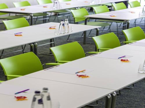 a row of tables in a classroom with green chairs at ibis Styles Zeebrugge in Zeebrugge
