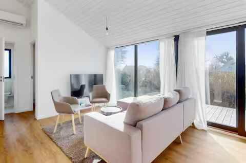 a living room with a white couch and windows at Stylish Cottage Near Beach, Cliffs & Harbour in Havnelev
