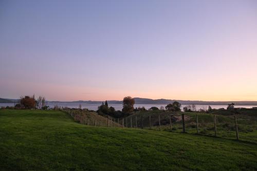 a field with a fence and a view of the water at Hamurana Lakeview Farmhouse Luxury Retreat in Hamurana