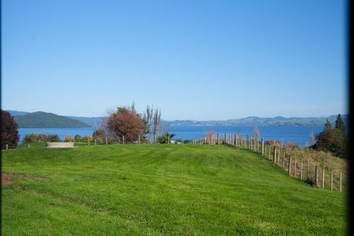 a grassy hill with a fence in front of a lake at Hamurana Lakeview Farmhouse Luxury Retreat in Hamurana