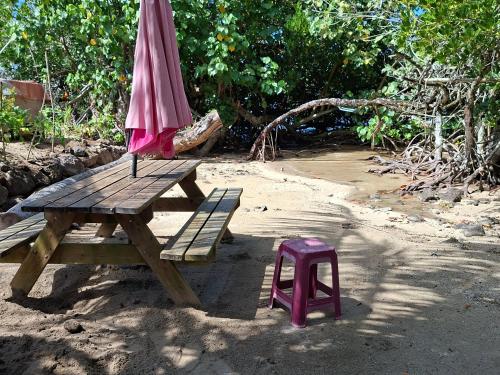 a wooden picnic table with a pink umbrella and a stool at Tehuarupe Surf Studio 2 in Haapiti