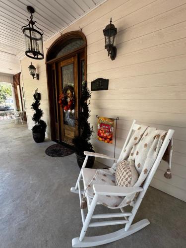 a white rocking chair on a porch with a door at Opus House Historic Natchitoches in Natchitoches