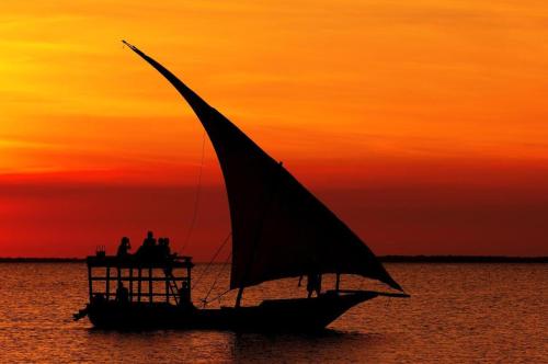 a boat with a sail in the water at sunset at Miramont Club Villas in Nungwi