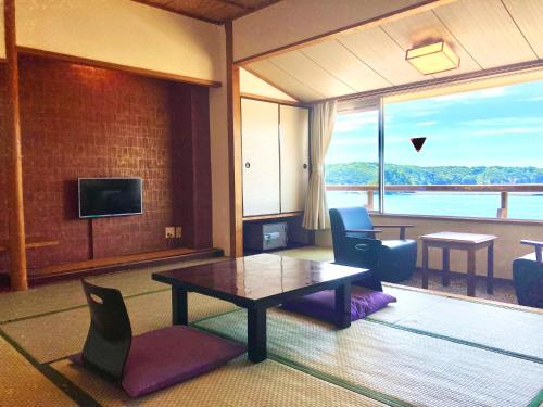 a living room with a table and chairs and a large window at Shimoda Itoen Hotel Hanamisaki in Shimoda