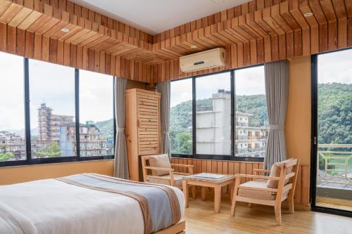a bedroom with a bed and chairs and windows at Trekkers Inn Boutique Hotel Pokhara in Pokhara