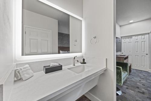 a white bathroom with a sink and a mirror at University Park Inn & Suites, an Ascend Collection Hotel in Davis