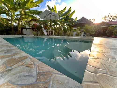 a swimming pool with an umbrella next to a house at Zanzllywood Uroa Beach Apartments in Dikoni