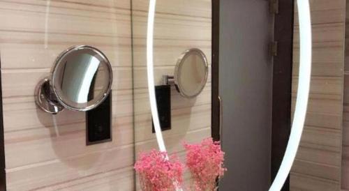 a mirror on a wall with a vase with pink flowers at Xana Hotelle· Tianjin Railway Station Jinwan Square Binjiang Avenue in Tianjin