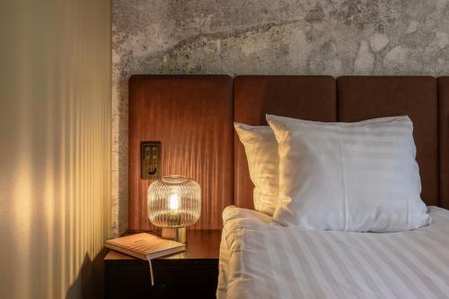 a bed with a lamp and a book on a night stand at H28 - Hotel, Apartments and Suites by UHANDA in Tampere