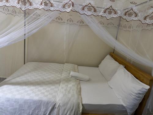 Un dormitorio con una cama con dosel con sábanas y almohadas blancas. en Ciara's Home Entebbe, en Entebbe