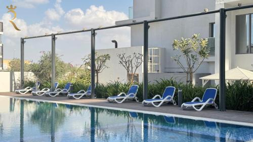 a row of lounge chairs next to a swimming pool at Serenity Mirage - Elegant 2BR Duplex Retreat with Pool in Oasis, Near Masdar City in Al Qurayyah