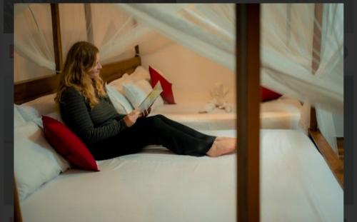 a woman sitting on a bed reading a book at Rainforest Holiday Inn in Deniyaya