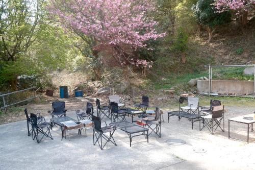 a group of chairs and tables and a tree with pink flowers at ARUYOguesthouse 一棟貸切 大人数でbbqと焚き火を楽しむ in Haibara
