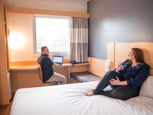 a man and a woman sitting on a bed in a hotel room at ibis Itu Plaza Shopping in Itu