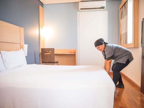 a woman bending over a bed in a hotel room at ibis Itu Plaza Shopping in Itu