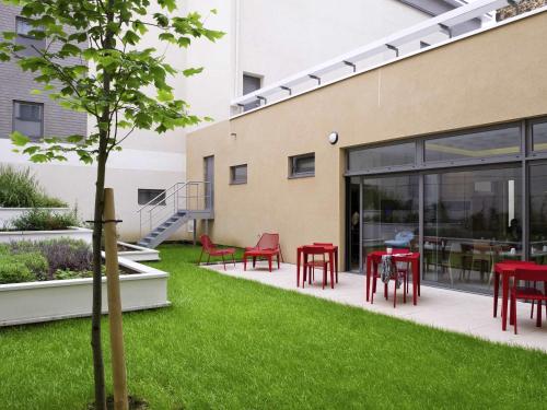 un jardin avec des tables et des chaises rouges à côté d'un bâtiment dans l'établissement Aparthotel Adagio Paris Vincennes, à Vincennes