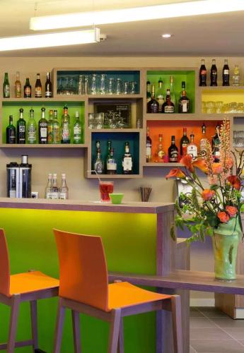 a bar with orange and green chairs and bottles at ibis Styles Périgueux Trélissac in Trélissac
