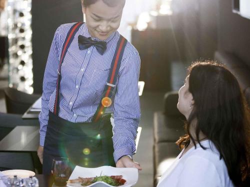 a man in a bow tie holding a plate of food at Novotel Basel City in Basel