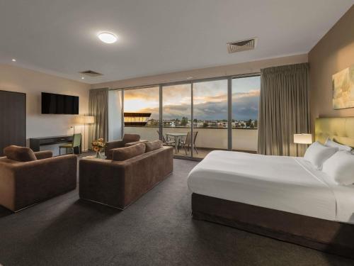 a hotel room with a bed and chairs and a balcony at Mercure Melbourne Caroline Springs in Caroline Springs