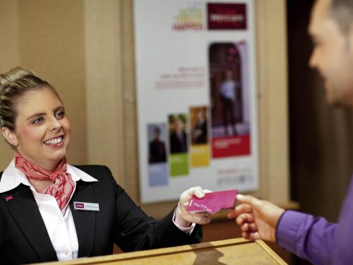 a woman in a suit handing a person a pink wallet at Mercure Tunbridge Wells Hotel in Royal Tunbridge Wells