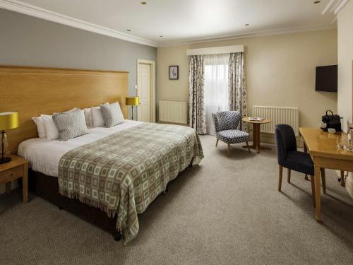 a hotel room with a bed and a desk and chairs at Mercure Gloucester Bowden Hall Hotel in Gloucester